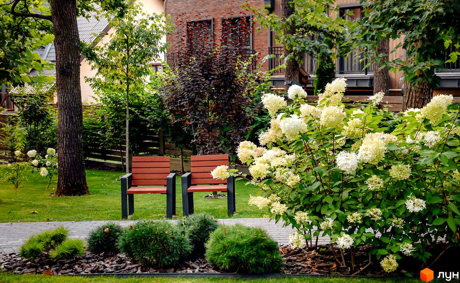 Котеджне містечко Oak Grove Town: фасад цегляного будинку з балконами та великими вікнами. Прибудинкова територія з газоном, деревами та квітучими кущами.