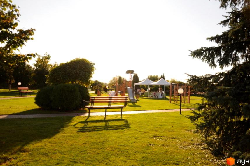 Зовнішній вигляд прибудинкової території житлового комплексу КМ Вишневе містечко з зеленими насадженнями та зонами відпочинку.