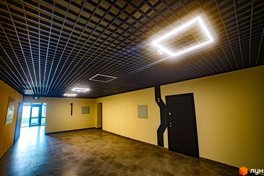 Комплекс Сонячний: сучасний під'їзд з квадратними світильниками та дверима під номер 3. Оздоблення стін та підлоги виконано в нейтральних тонах.