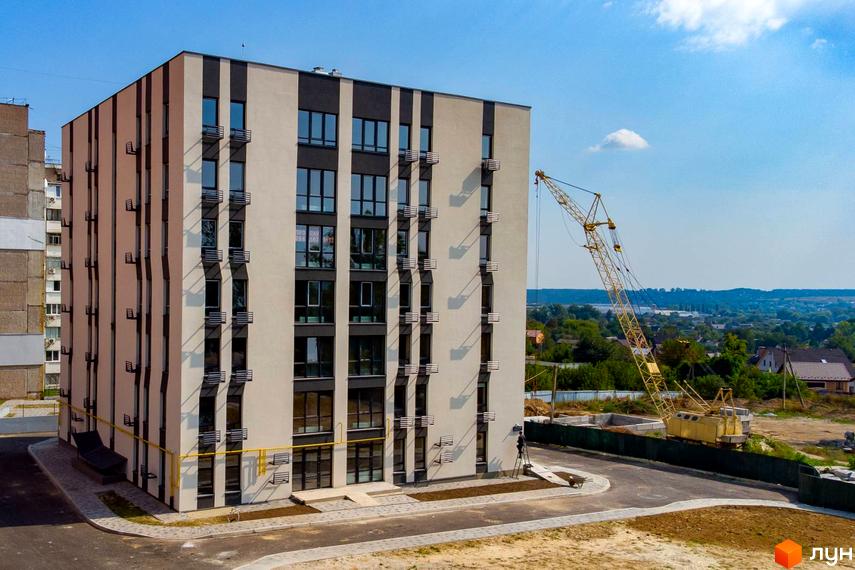 Новобудова ЖК Сонячний з фасадом в бежево-чорних тонах та балконами, поруч будівельний кран та прибудинкова територія.