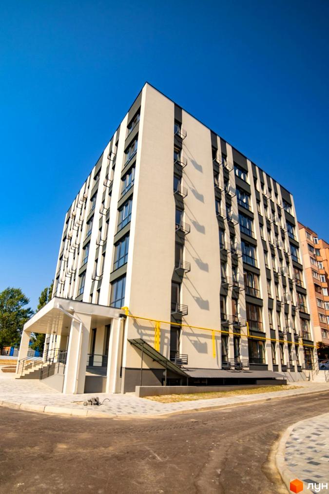 Зовнішній вигляд будинку ЖК Сонячний з вікнами та кондиціонерами, що виходить на прибудинкову територію з бруківкою та дорогою.