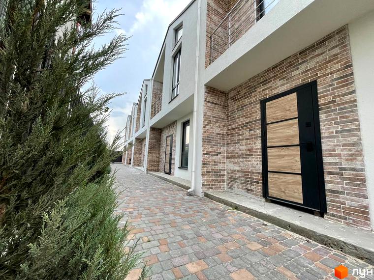 Таунхауси West Homes з цегляним фасадом та дерев'яними елементами, розташовані вздовж вимощеної бруківкою алеї.