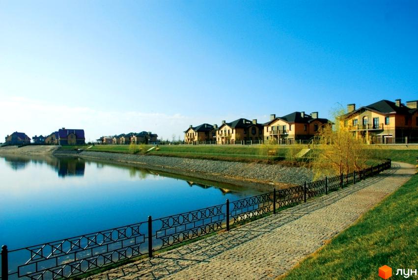 Котеджне містечко КМ Вишневе містечко з озером та доглянутою прибудинковою територією. Будинки з цегляним фасадом та темними дахами розташовані вздовж водойми.