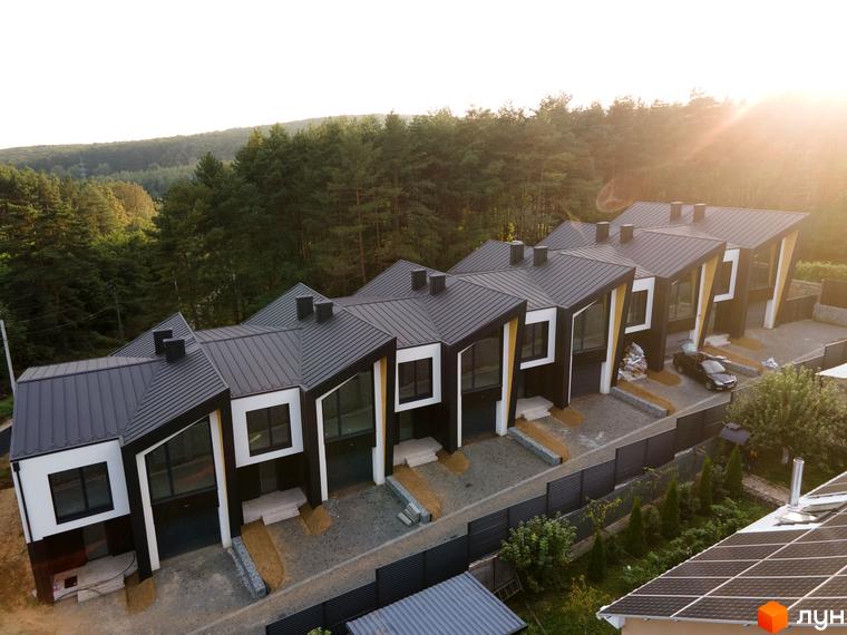 Таунхаус „ДЖЕРЕЛЬНА“: сучасні будинки з темними дахами та великими вікнами, оточені зеленню та облаштованою прибудинковою територією.
