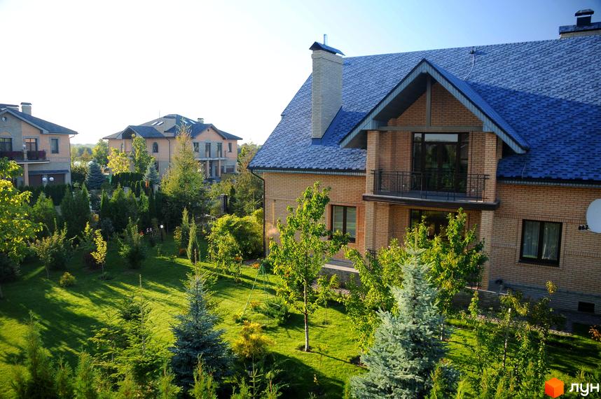 Котеджне містечко Вишневе містечко. Цегляні будинки з синім дахом та доглянутою прибудинковою територією з газоном та деревами.