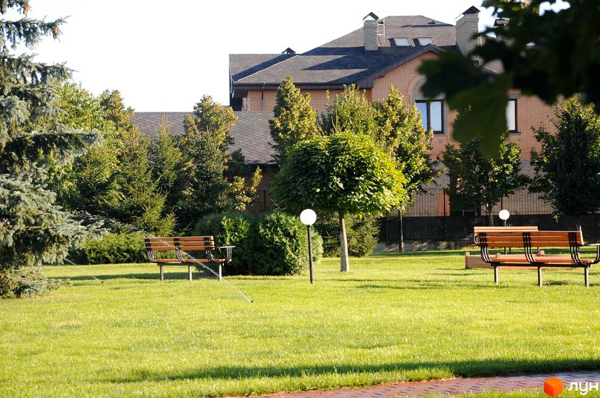 Котеджне містечко КМ Вишневе містечко. Зелена прибудинкова територія з лавками та газоном. Цегляний будинок з темним дахом.