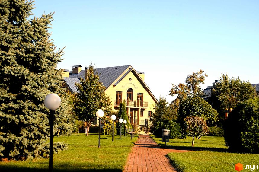 Котеджне містечко Вишневе містечко: жовтий цегляний будинок з балконами та темним дахом. Доглянута прибудинкова територія з газоном, доріжкою з бруківки та освітленням.