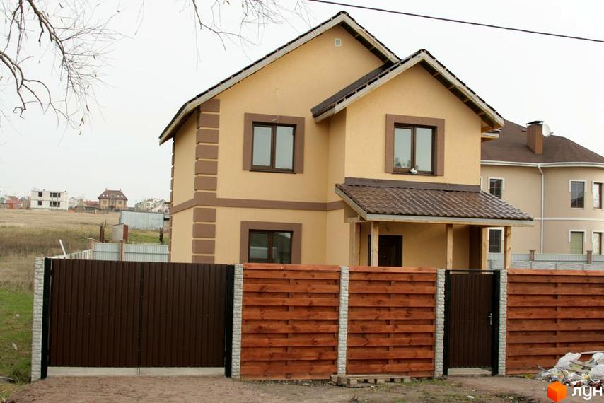 Котеджне містечко КМ Happy Land: двоповерховий будинок світло-бежевого кольору з коричневими декоративними елементами та коричневим дахом. Прибудинкова територія огороджена дерев'яним та металевим парканом.