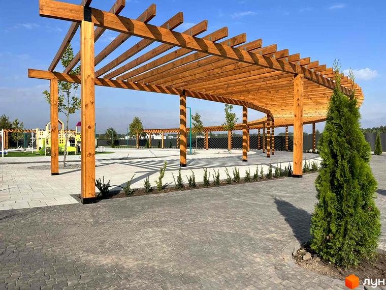 Дерев'яна альтанка на території Містечка котеджів Beverly Hills Residence. Видно бруківку, зелені насадження та дитячий майданчик на задньому плані.