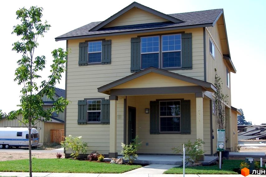 Зовнішній вигляд двоповерхового будинку з світло-жовтим фасадом, зеленими віконницями та сірим дахом. На прибудинковій території є дерева та зелений газон.