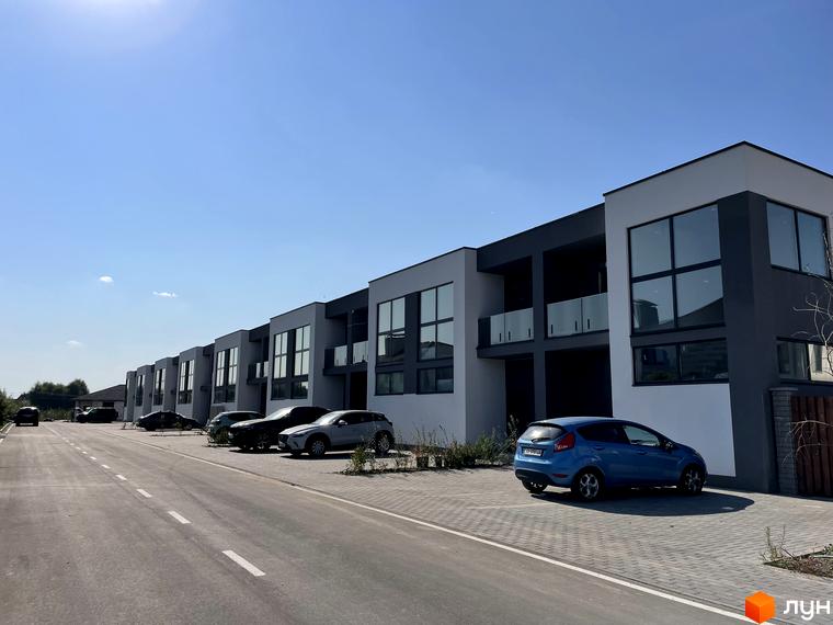 Котеджне містечко КМ Osocor House з сірими фасадами та великими вікнами, паркуванням та дорогою перед будинками.