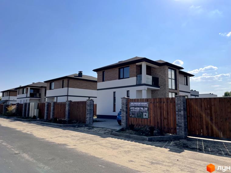 Котеджне містечко КМ Osocor House з дерев'яними парканами та цегляними стовпами. Сучасні двоповерхові будинки з коричневою та білою обробкою.
