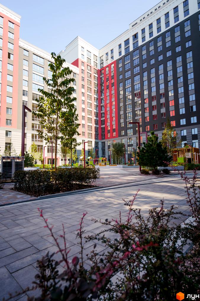 Житловий комплекс Irpin City з фасадами в сіро-червоних тонах. Внутрішній двір з бруківкою, деревами та дитячим майданчиком.