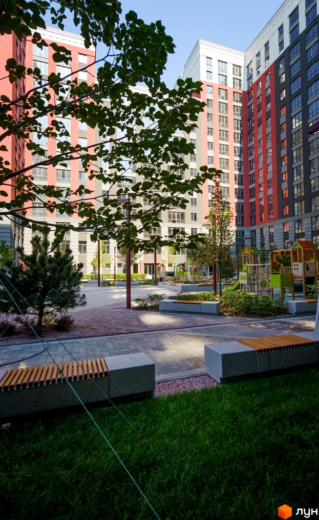 Житловий комплекс Irpin City з фасадами в червоних та сірих тонах. На прибудинковій території розташовані дитячі майданчики та зони відпочинку з лавками.
