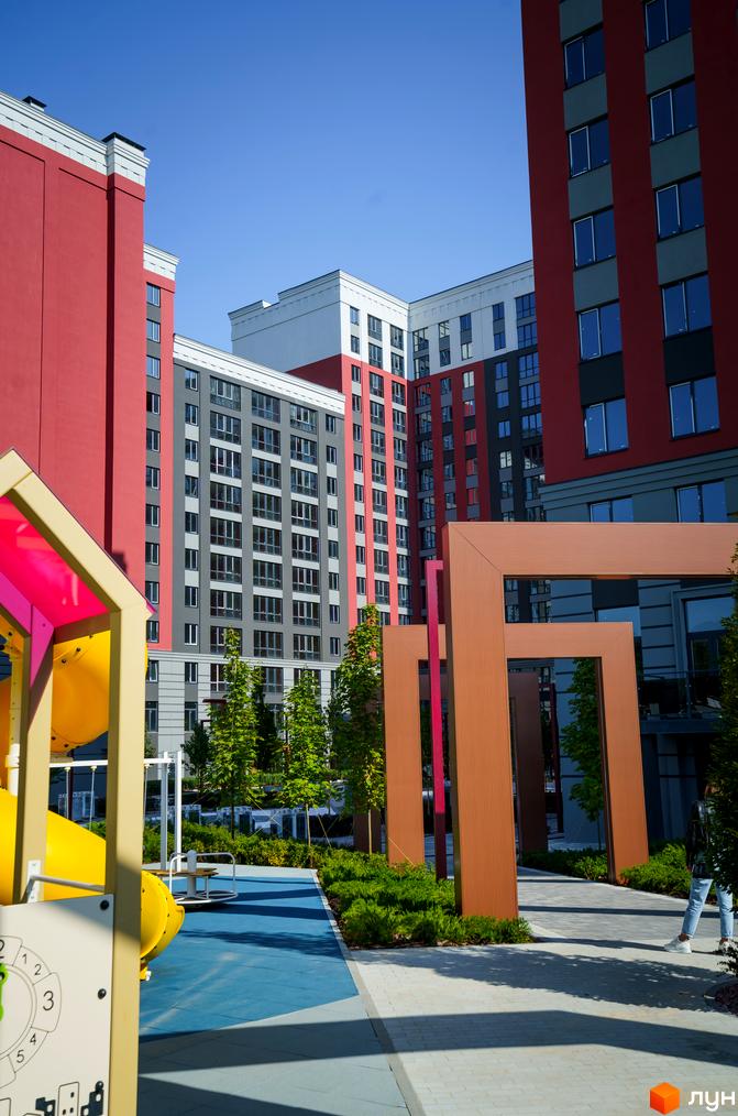 Житловий комплекс Irpin City з яскравими фасадами на тлі блакитного неба. На території комплексу розташований дитячий майданчик та зелені насадження.