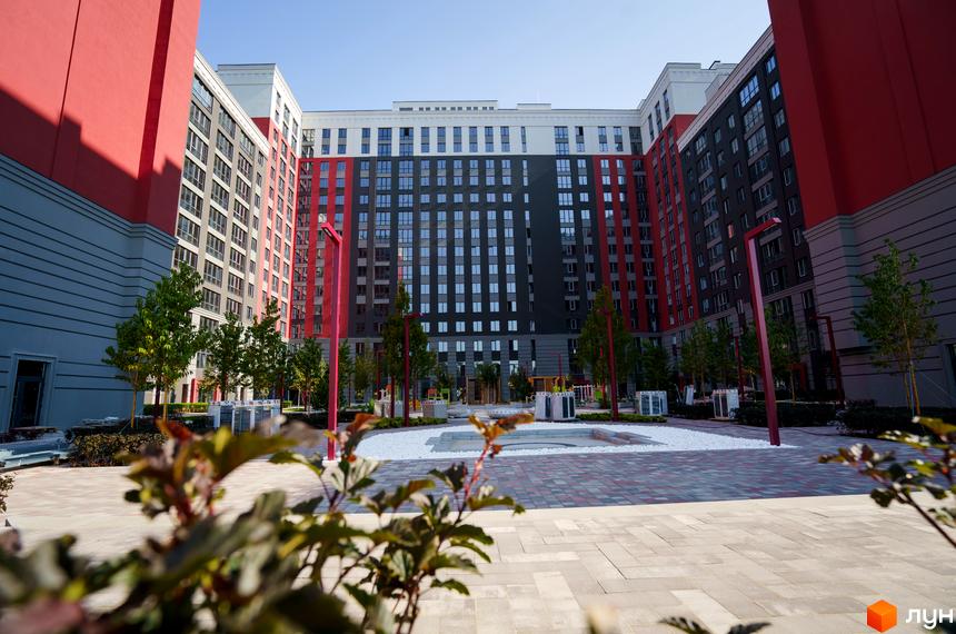 Житловий комплекс Irpin City з червоними та сірими фасадами, вікнами та прибудинковою територією з бруківкою та зеленими насадженнями.