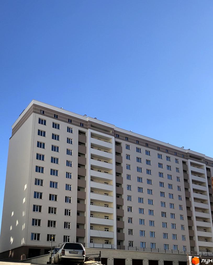 Зображення багатоповерхового будинку в Житловому районі Новобудова. На фото видно фасад будівлі та припаркований автомобіль.
