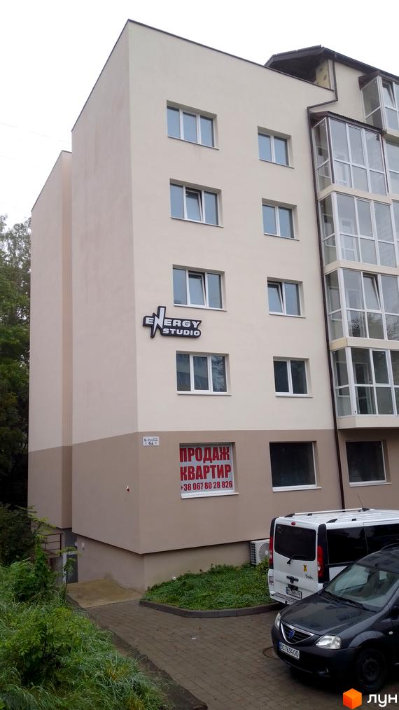 Зовнішній вигляд будинку Energy Studio з великими вікнами та вивіскою, перед яким припарковані автомобілі та є невелика зелена зона.