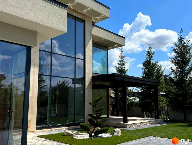 Зовнішній вигляд будинку з великими вікнами в Котеджному містечку Riviera City Park. Навколо зелена галявина та декоративні дерева.