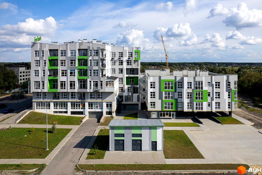 Новобудова ЕкоПарк: багатоповерхові будинки сіро-білого кольору із зеленими елементами на фасадах. Територія має зелені зони та доріжки.