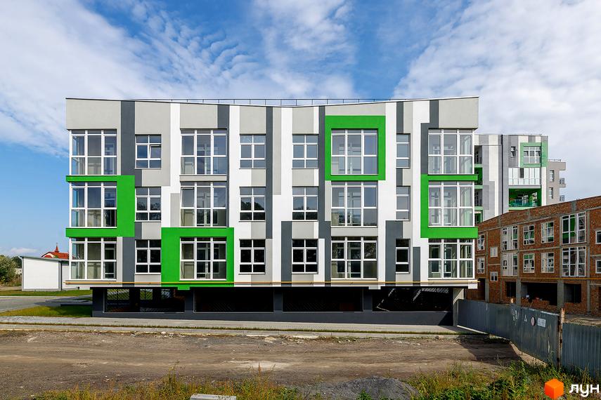 Житловий комплекс ЕкоПарк з фасадом у смужку сірих, білих та зелених кольорів. Поруч видно будівельний майданчик.