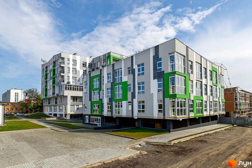 Будівельний проєкт ЕкоПарк з яскравими зеленими елементами на фасаді та сірими вставками. Навколо будинку облаштований доглянутий двір з газоном та вимощеною плиткою територією.