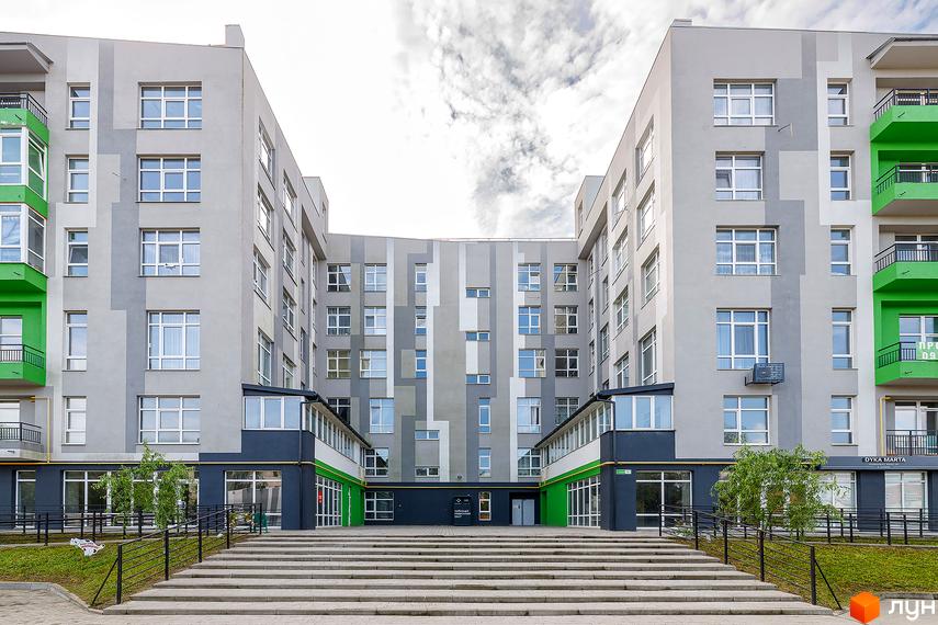 Зовнішній вигляд новобудови ЖК ЕкоПарк з сірими та зеленими фасадами, великою кількістю вікон та балконів. Перед будинком розташовані сходи та зелена зона.