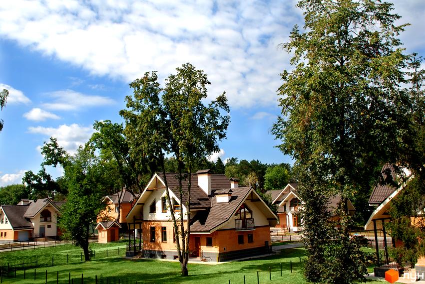 Зовнішній вигляд будинків комплексу КМ Ясні Зорі, оточених зеленими деревами та прибудинковою територією.