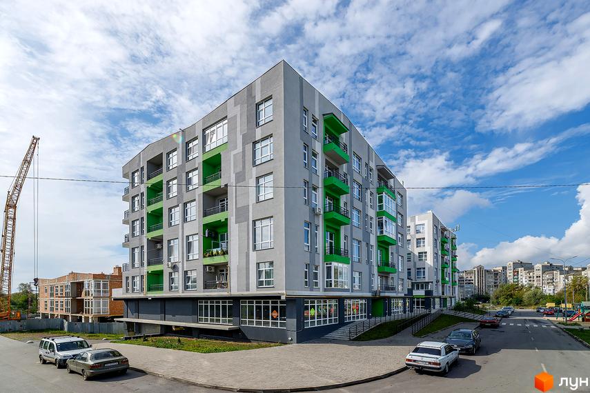 Житловий комплекс ЕкоПарк з сірими фасадами та яскравими зеленими балконами. Поруч дорога з автомобілями та будівельний кран.