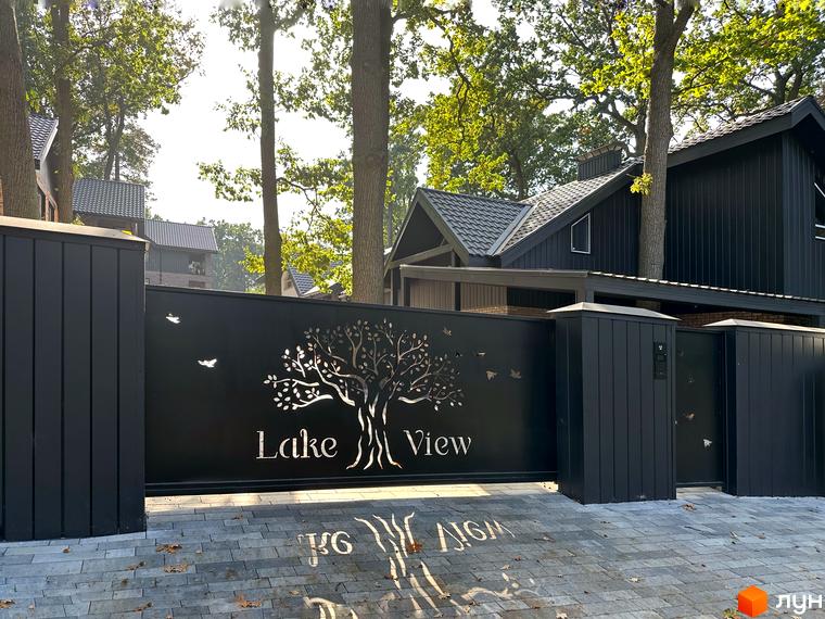 В'їзд до котеджного містечка Lake View з елегантною брамою та вишуканим ландшафтом. На брамі зображено дерево життя та птахів.