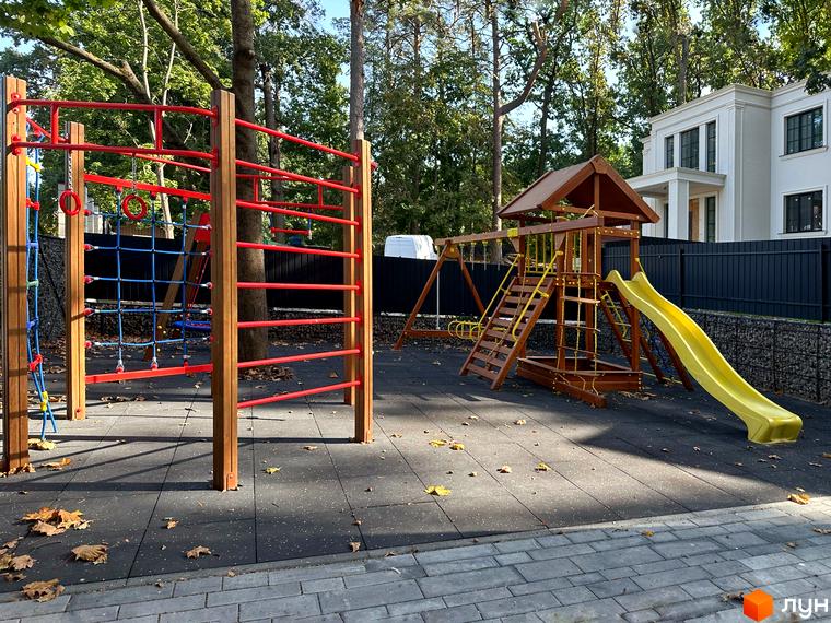 Дитячий майданчик з гіркою та гойдалками на території Котеджного містечка Lake View. Двоповерховий будинок позаду.