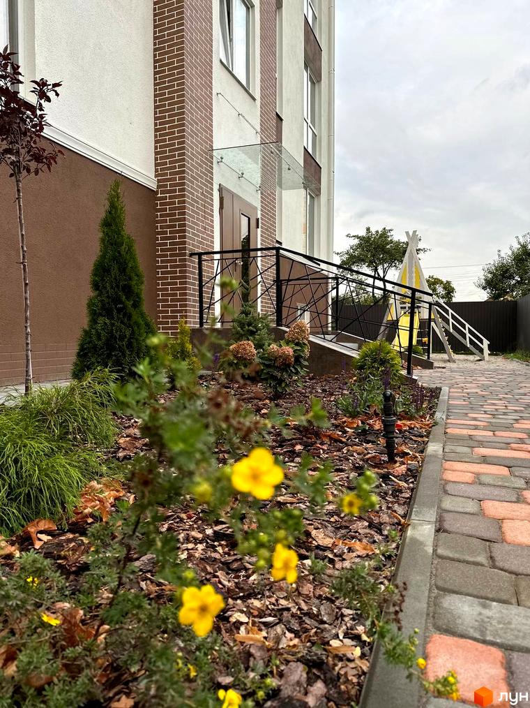 Житловий комплекс SMART IDEA: фасад будівлі з цегляними елементами та прибудинкова територія з дитячим майданчиком та зеленими насадженнями.