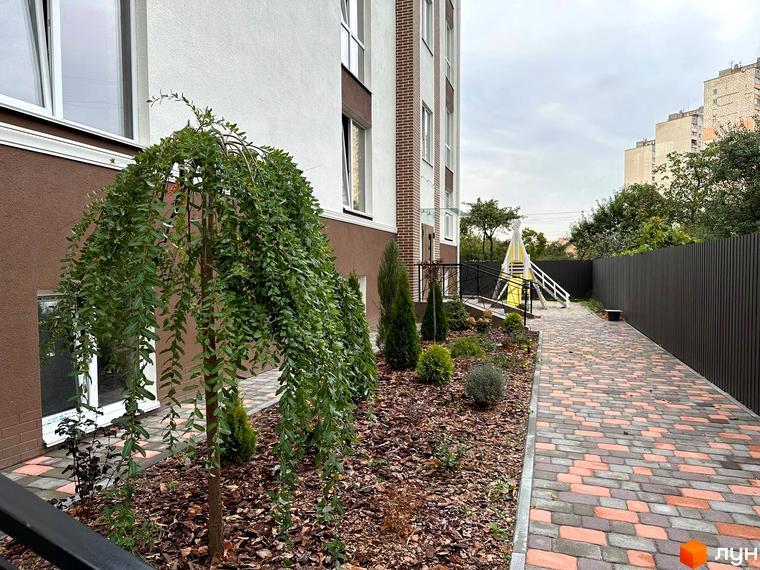 Житловий комплекс SMART IDEA: фасад будинку та доглянута прибудинкова територія з доріжкою та зеленими насадженнями.