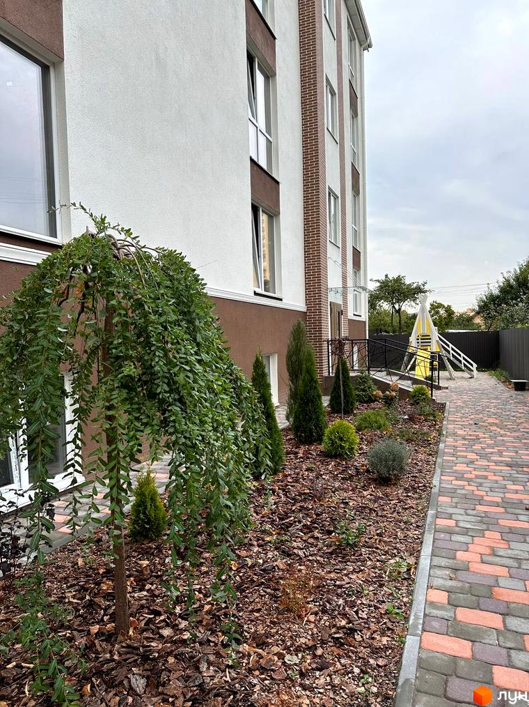 Зовнішній вигляд будинку ЖК SMART IDEA з цегляними вставками та доглянутою прибудинковою територією з деревами та доріжками.