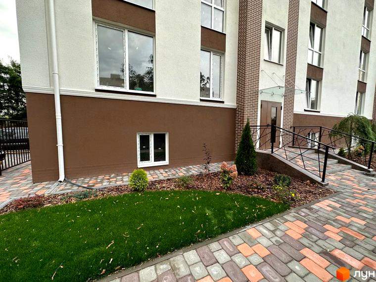 Зовнішній вигляд новобудови ЖК SMART IDEA з цегляними вставками та доглянутою прибудинковою територією з газоном та бруківкою.