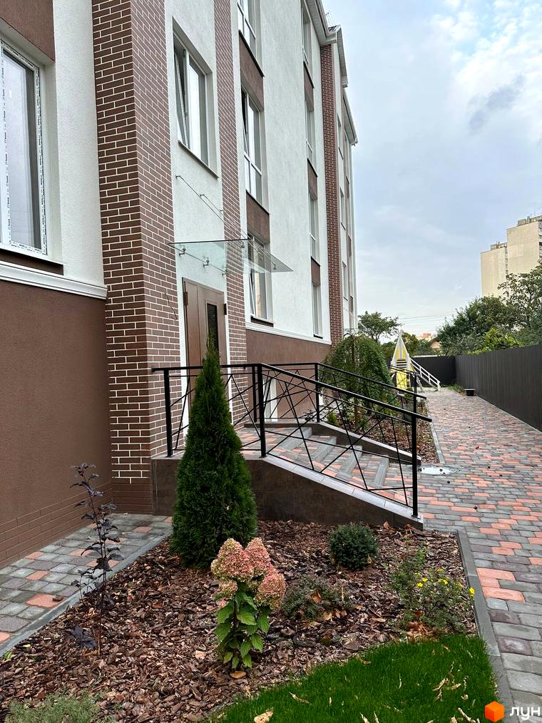 Зовнішній вигляд новобудови ЖК SMART IDEA з цегляним оздобленням та прибудинковою територією з бруківки та зелених насаджень.