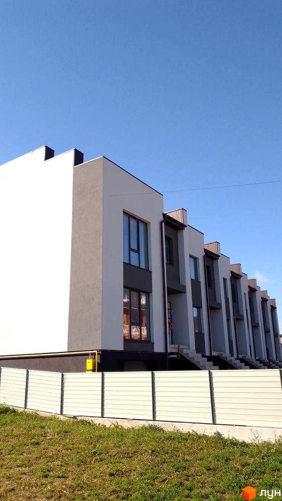 Будівля житлового комплексу на вулиці Петриківській, 12, з біло-сірим фасадом та великими вікнами. Попереду розташована огорожа та зелена ділянка.