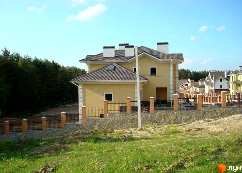 Будинок житлового комплексу КМ Іванковичі з жовтою фасадною стіною та черепичним дахом. Прибудинкова територія з огорожею та зеленими насадженнями.