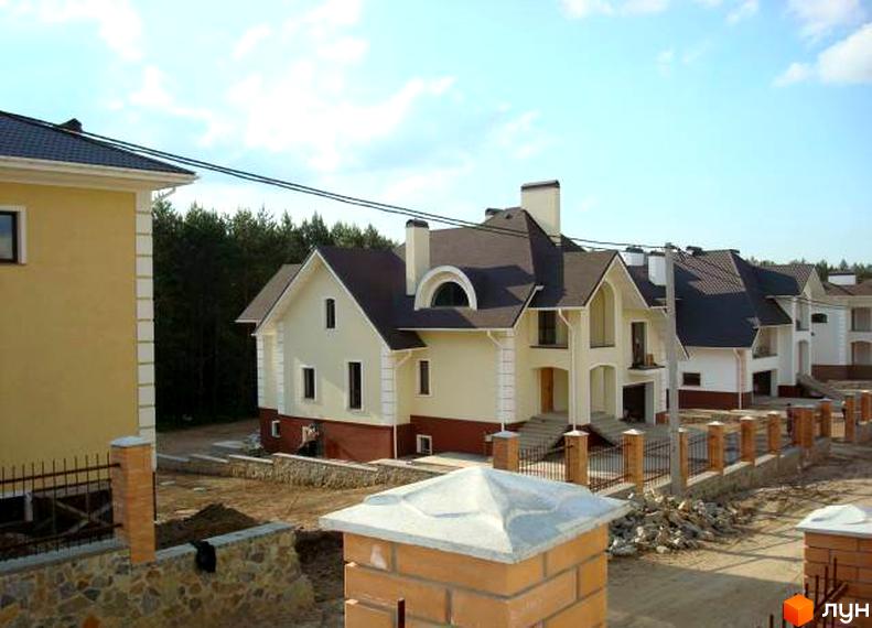 Фото Котеджного містечка Іванковичі: двоповерхові будинки з темними дахами та світлим фасадом, огороджені парканом. Навколо новобудови зелені дерева.