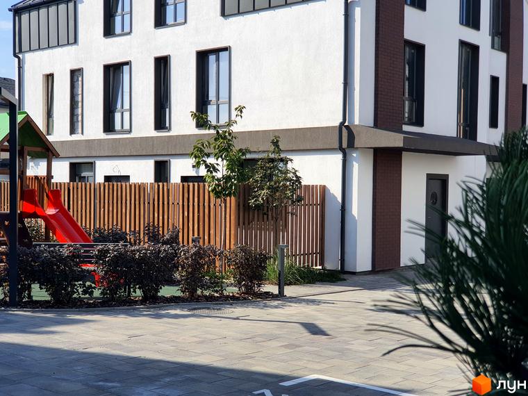 Таунхауси New Smart 6: фасад будівлі з цегляними вставками, вікнами та дитячим майданчиком із червоною гіркою.