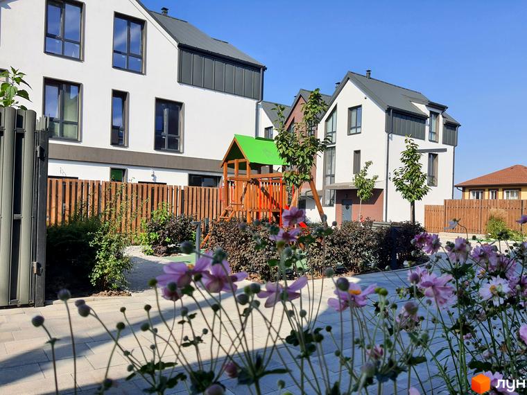 Таунхауси New Smart 6: білі фасади з темними вікнами та сірими дахами. Прибудинкова територія з дитячим майданчиком та квітами.