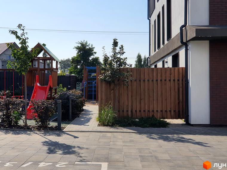 Таунхауси New Smart 6: фасад будівлі та дитячий майданчик з червоною гіркою. Прибудинкова територія з дерев'яним парканом та бруківкою.