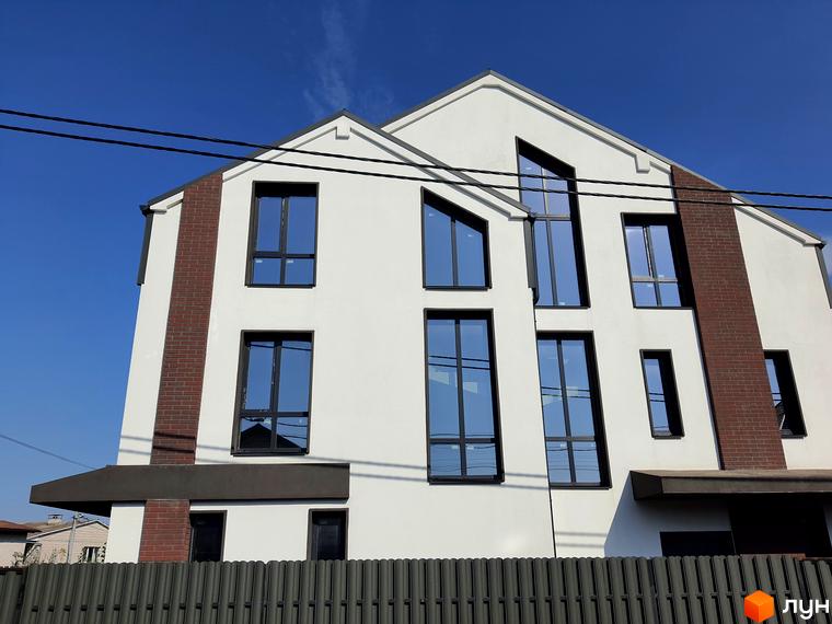 Фасад житлового комплексу New Smart 6 з великими вікнами та цегляними елементами на тлі блакитного неба. Огороджена територія з парканом.