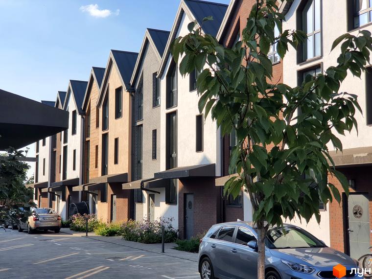 Таунхауси New Smart 6 з цегляним та штукатурним фасадом, розташовані вздовж асфальтованої дороги з прибудинковою територією та деревами.