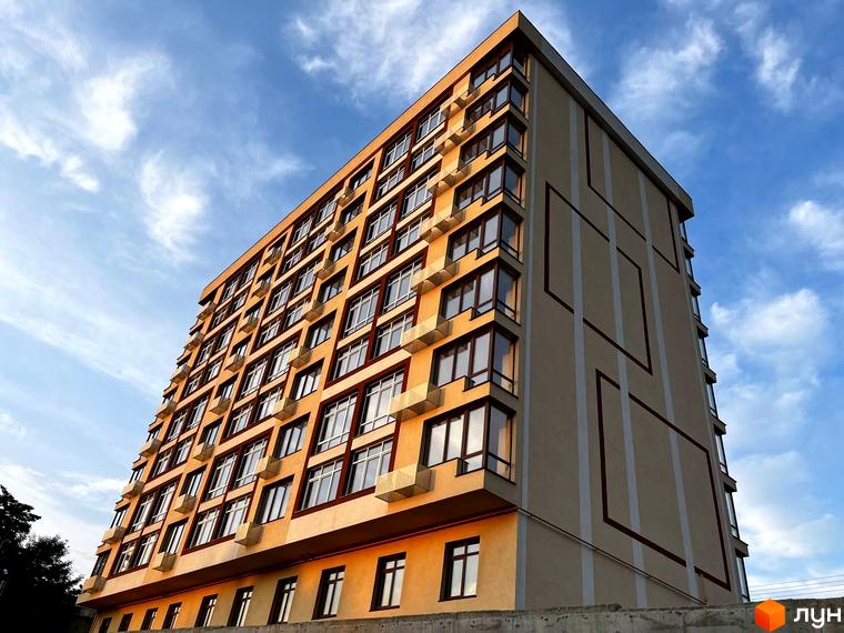 Вигляд багатоповерхового будинку з великою кількістю вікон у Житловому комплексі „Фортечний“ на фоні блакитного неба.