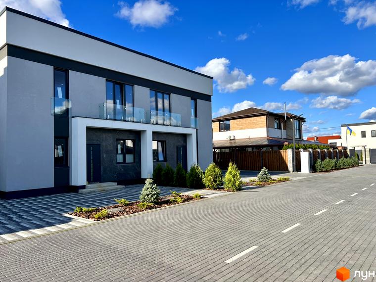 Зовнішній вигляд новобудови КМ GREAT OSOCOR Apartments з сірим фасадом та скляними балконами. Прибудинкова територія з бруківкою та зеленими насадженнями.