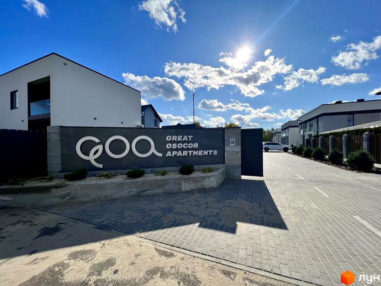 Котеджне містечко GREAT OSOCOR Apartments з білими будинками та бруківкою перед в'їздом. Сонячний день з хмарами.