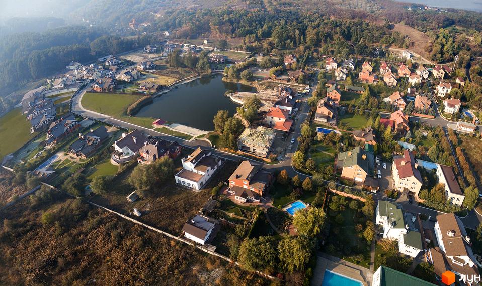 Вид на житловий комплекс КМ Альпійка з висоти, котеджі оточені зеленими територіями та водоймою.