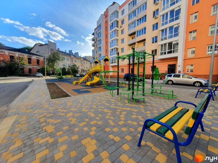 Новобудова Зоря: багатоповерховий будинок світлих та помаранчевих кольорів. Поруч облаштований дитячий майданчик з гірками та спортивними тренажерами.