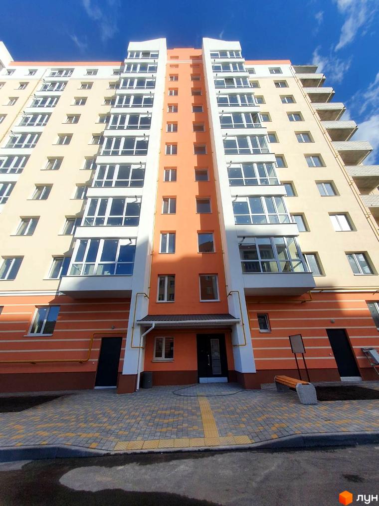 Житловий комплекс Зоря: багатоповерховий будинок з жовто-помаранчевим фасадом та великими вікнами. Прибудинкова територія має бруківку та лавку.